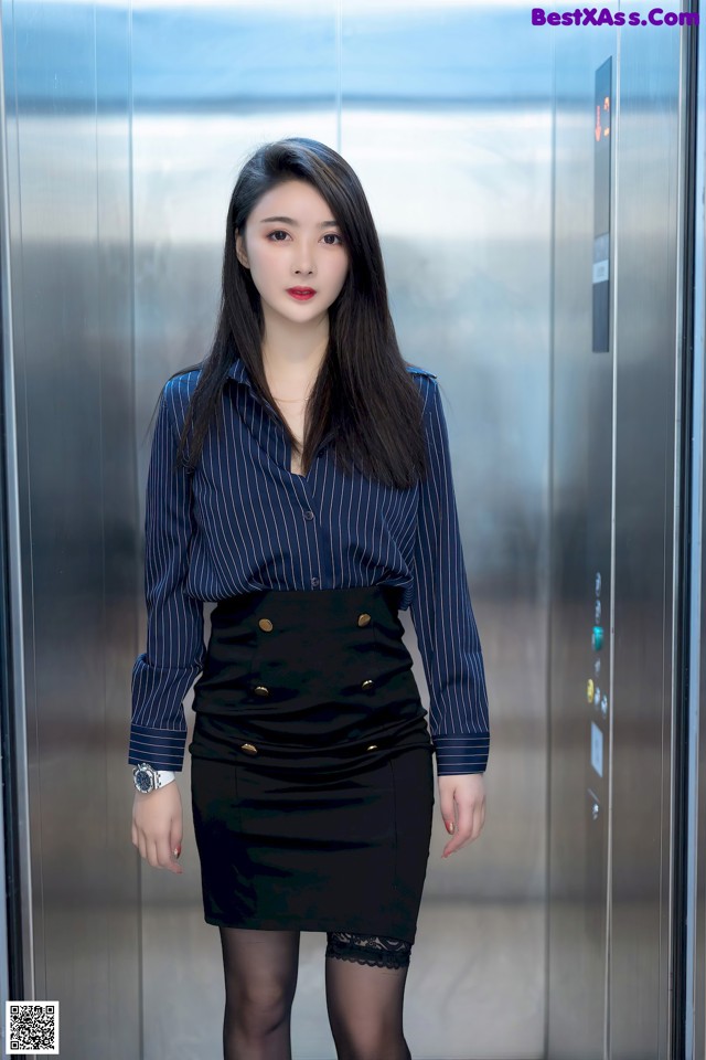 A woman in a blue shirt and black skirt standing in an elevator.